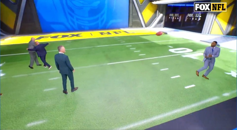 Four men on a green football field, with three of them appearing to struggle with each other, in a studio with a FOX NFL logo.