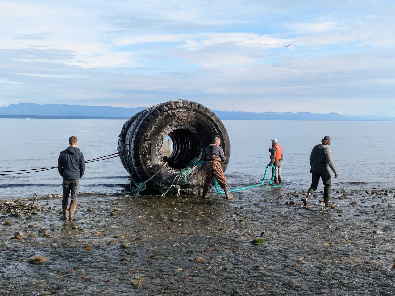 A few people gather near a giant tire on the beach, with the ocean in the background.