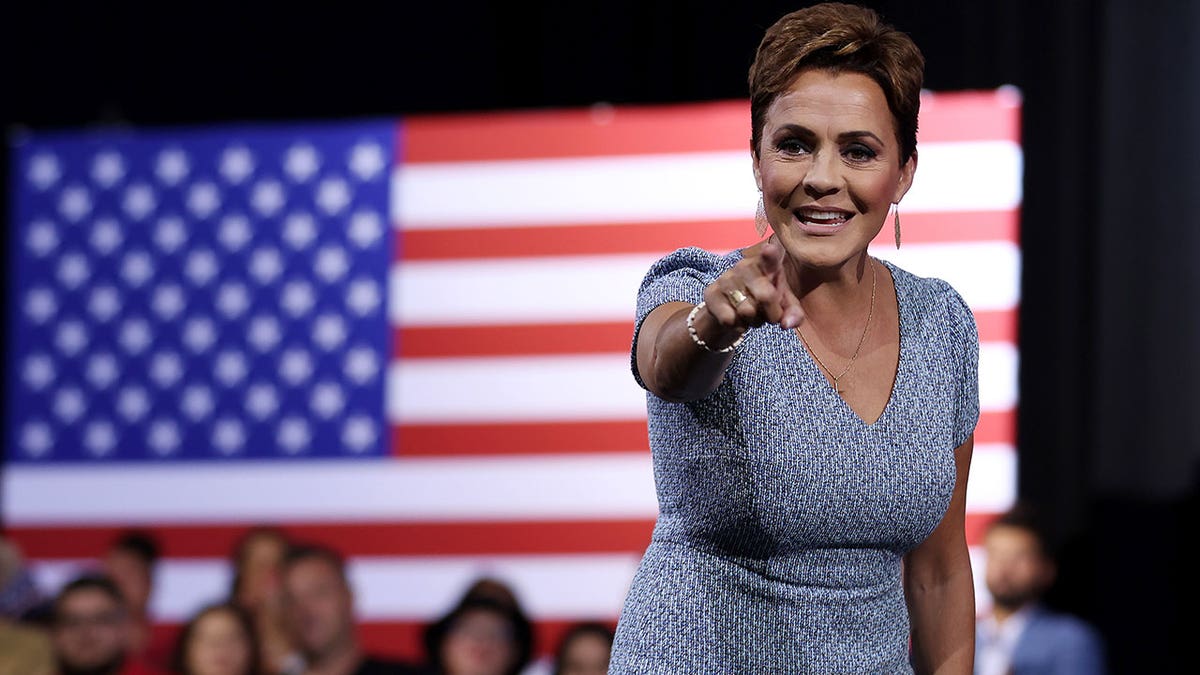 Acting U.S. Agency for Global Media VEP Kari Lake points at the camera with an American flag behind her.