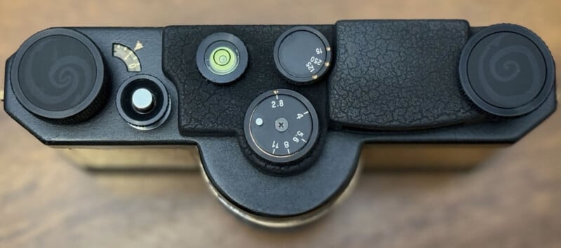 Top view of a vintage camera showing dials, buttons, and a level bubble for adjusting settings, all set against a wood surface.