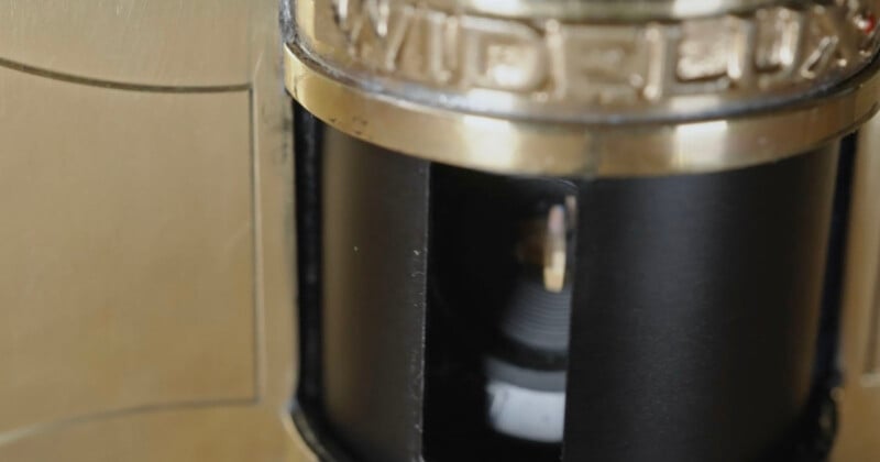 Close-up of a brass-colored combination lock with the dial partially visible through a small window, showing some internal mechanism and engraved lettering at the top.