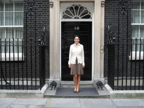 US Department of Justice A picture of Ghislaine Maxwell wearing a brown skirt and cream top standing outside Downing Street 