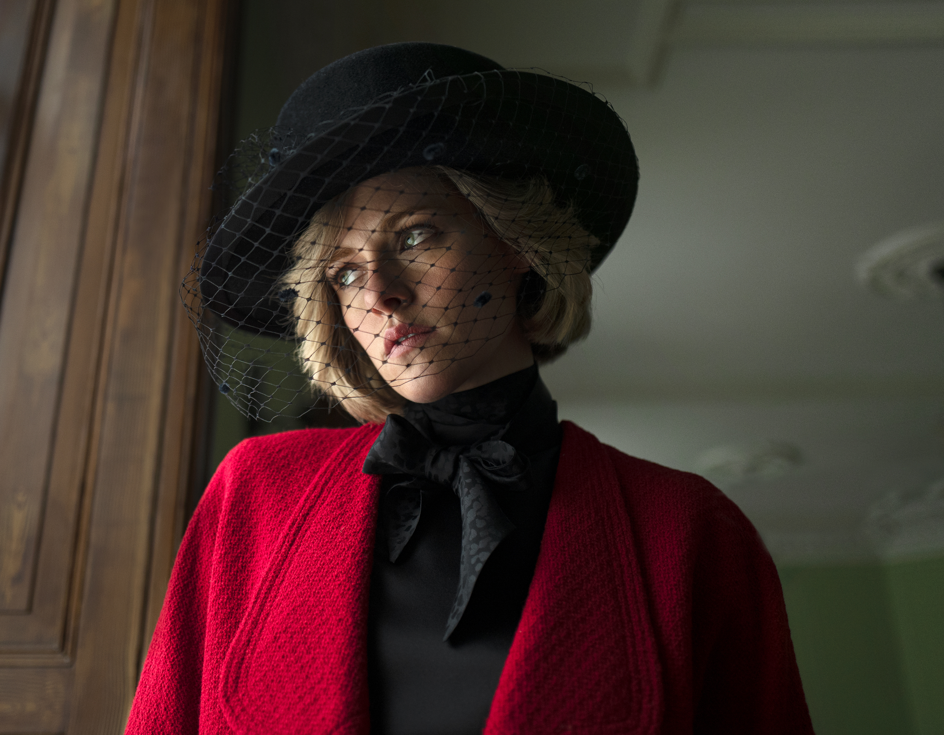 Kristen Stewart as Diana in "Spencer" wearing a black hat with a veil and a red sweater.