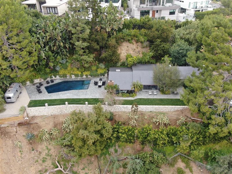 Aerial view of a modern home with a pool surrounded by greenery.
