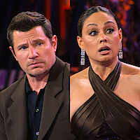 Nick and Vanessa Lachey dressed formally sit indoors, reacting with surprised and serious facial expressions, with colorful lights and abstract decor in the background.