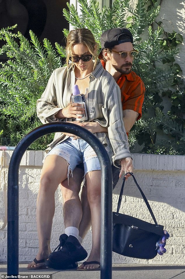 The 38-year-old former Disney Channel star sported shredded denim shorts with flip-flop sandals and certainly had her hands full - clutching a water bottle, iPhone and large black purse