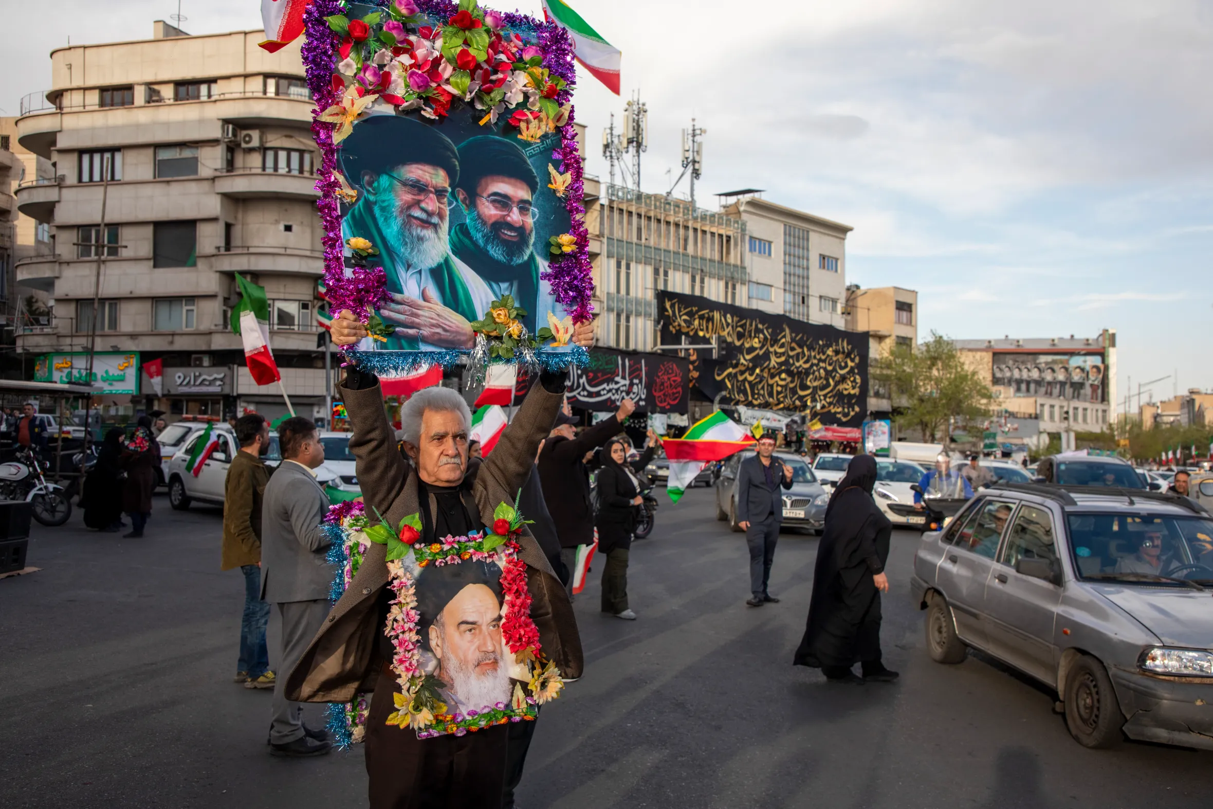 A man holding portraits of Ayatollah Ali Khamenei and Mojtaba Khamenei in Tehran's Enqelab Square.