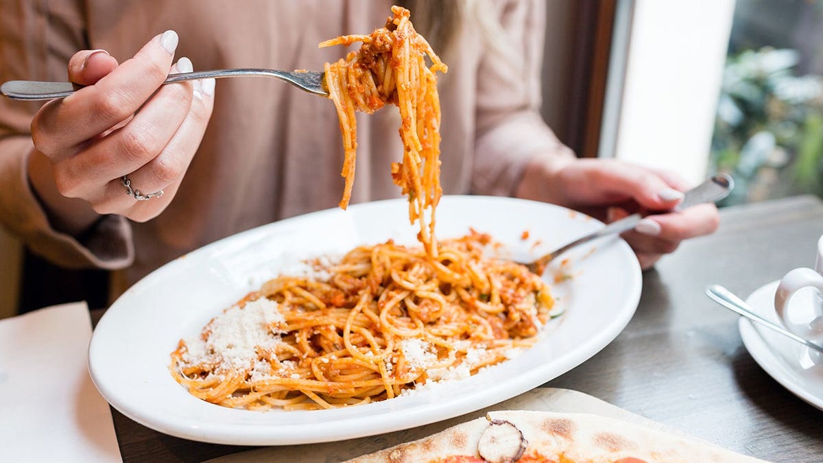 Girl eating spaghetti Bolognese pasta with tomato and meat using a fork and spoon