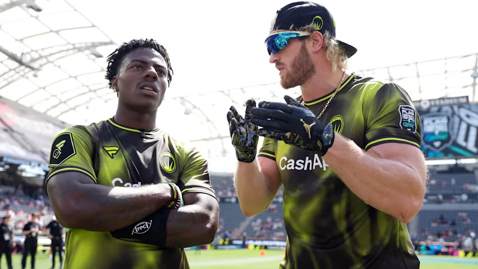 IShowSpeed and Logan Paul in matching green jerseys converse on a sports field.