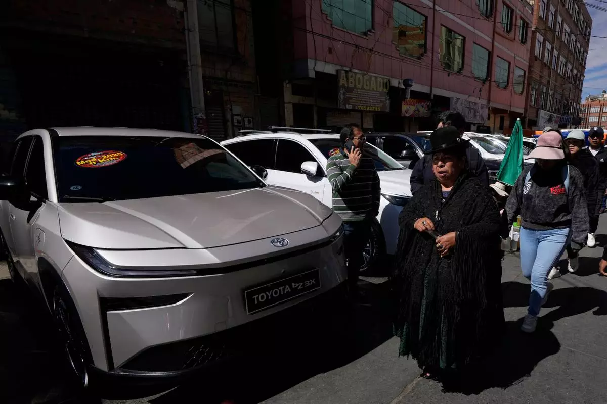 People walks past electric cars displayed for sale at "La Feria de la 16 de Julio," in El Alto, Bolivia, Sunday, April 19, 2026. (AP Photo/Juan Karita)